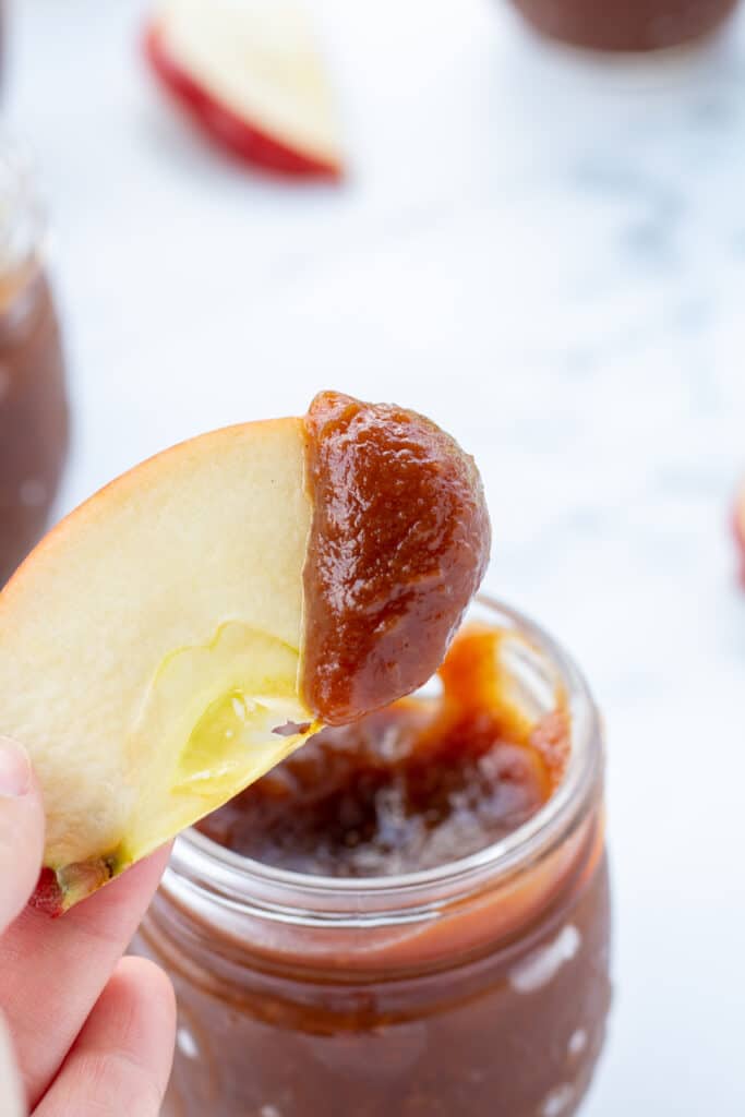 an-apple-slice-dipped-in-apple-butter-held-by-a-hand-over-a-glass-jar-of-apple-butter