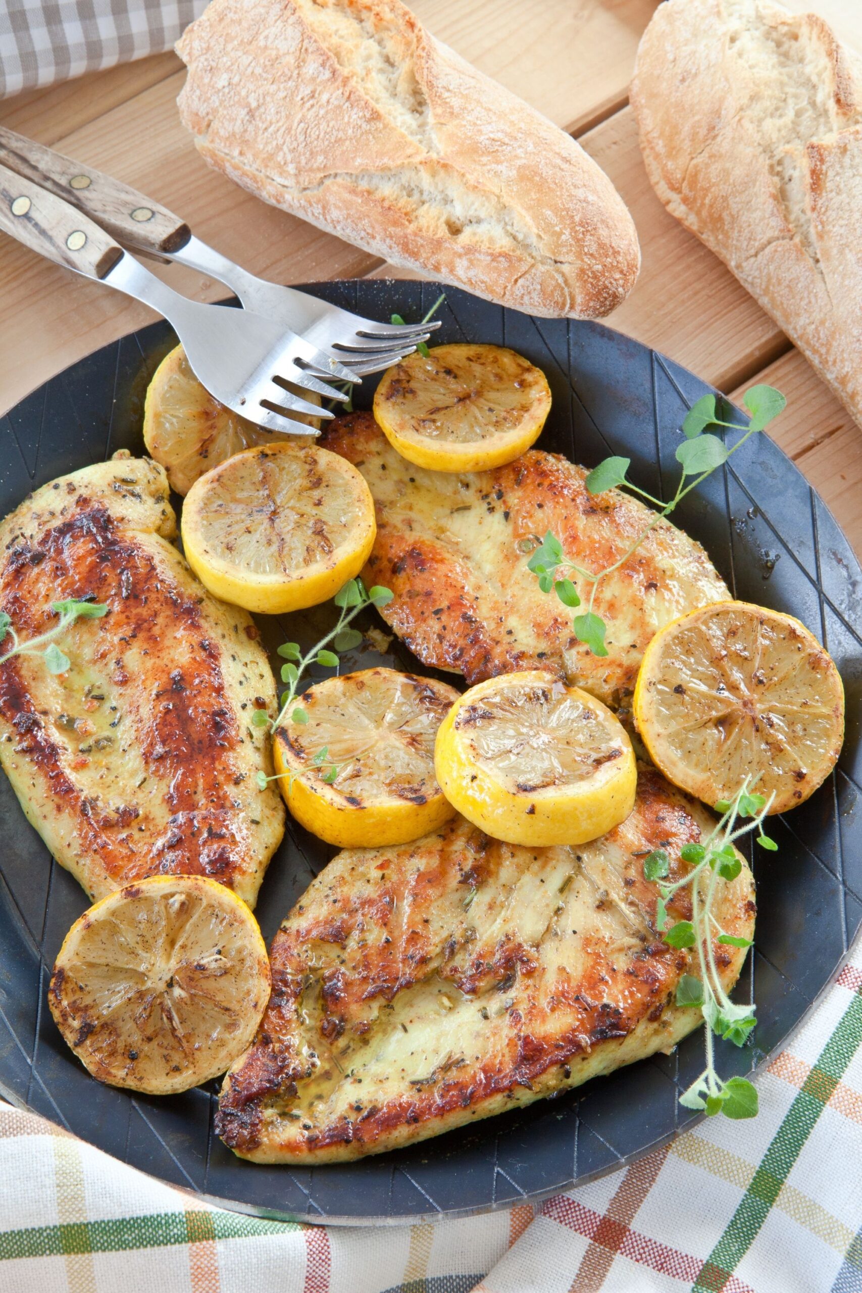 Chicken breasts on a plate with grilled lemons and green sprigs on top
