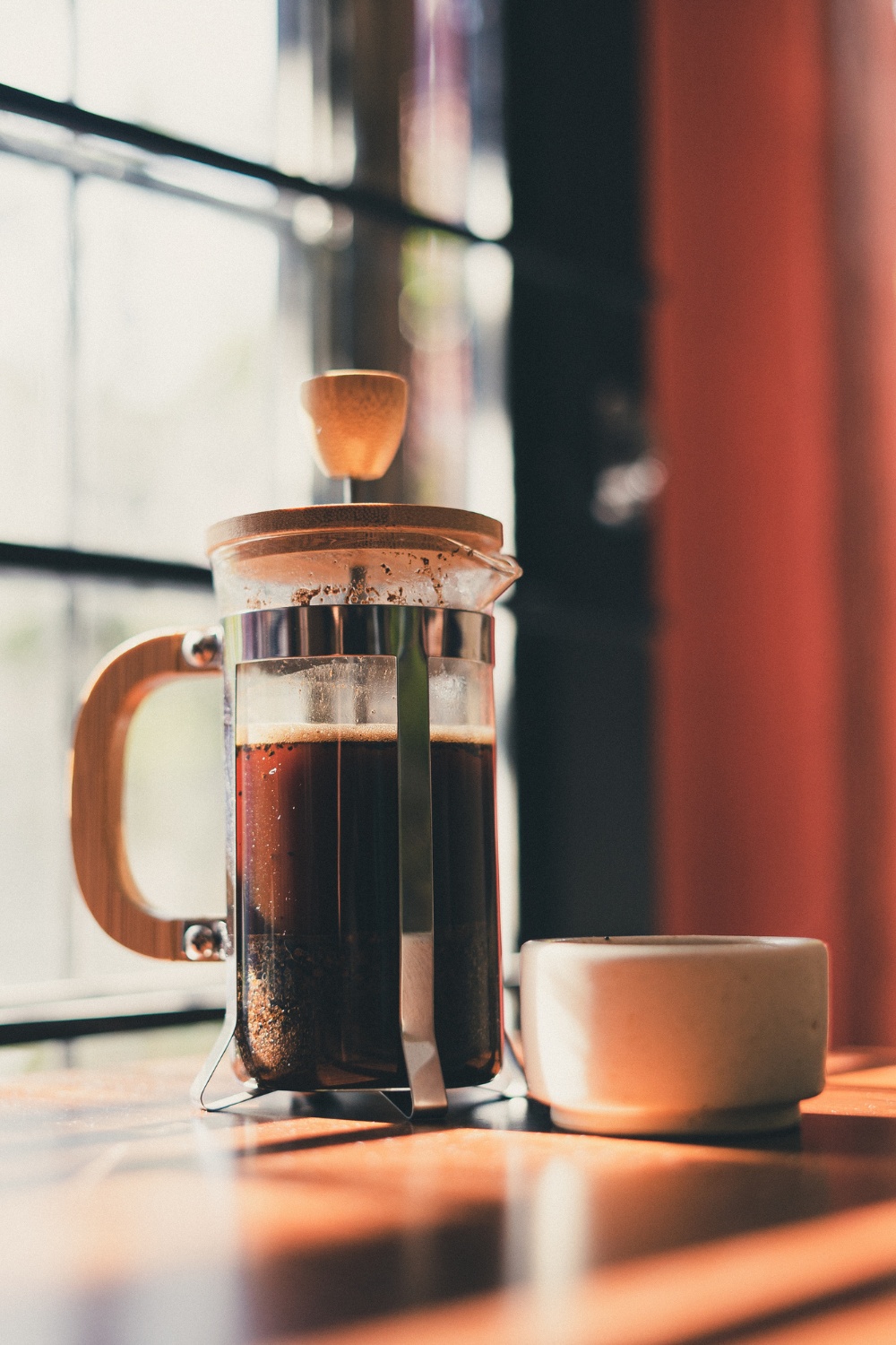 French press on a table next to a coffee cup 