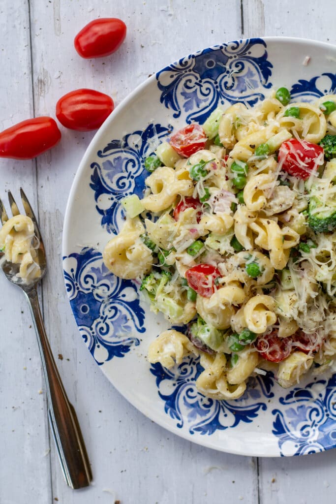 pasta salad on a blue and white plate with a fork on a white surface