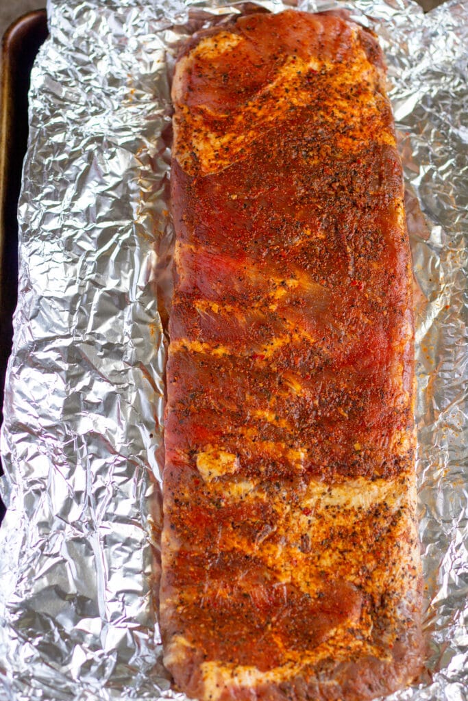 a rack of pork ribs on a sheet of aluminum foil covered with dry rub