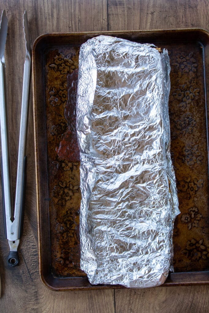 ribs wrapped with aluminum foil on a baking sheet