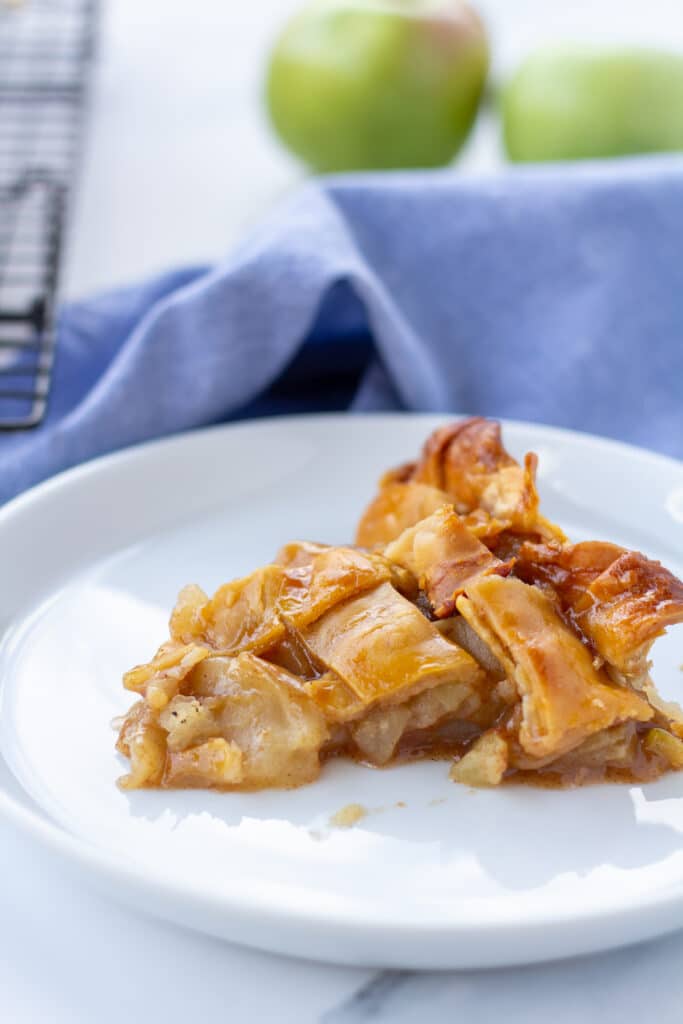 A slice of apple pie with a blue napkin and green apples in the background