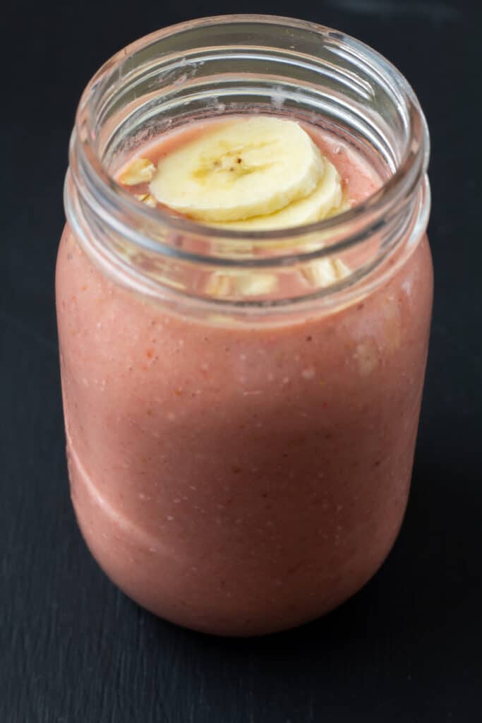 side view of a red smoothie with slice bananas and oats on top