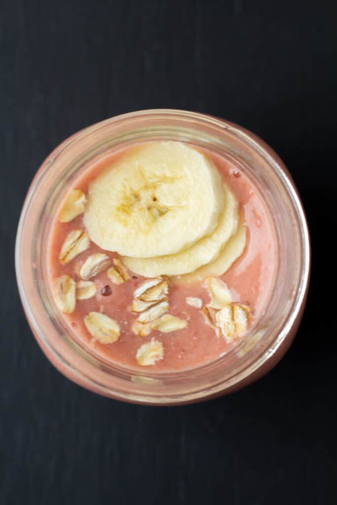 overhead shot of a smoothie with sliced bananas and oats on top