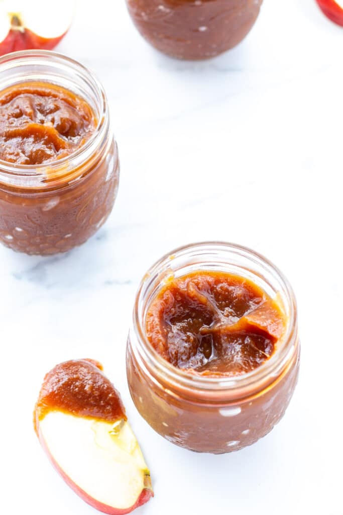 two-jars-of-apple-butter-and-one-apple-slice-dipped-in-apple-butter-on-a-white-counter