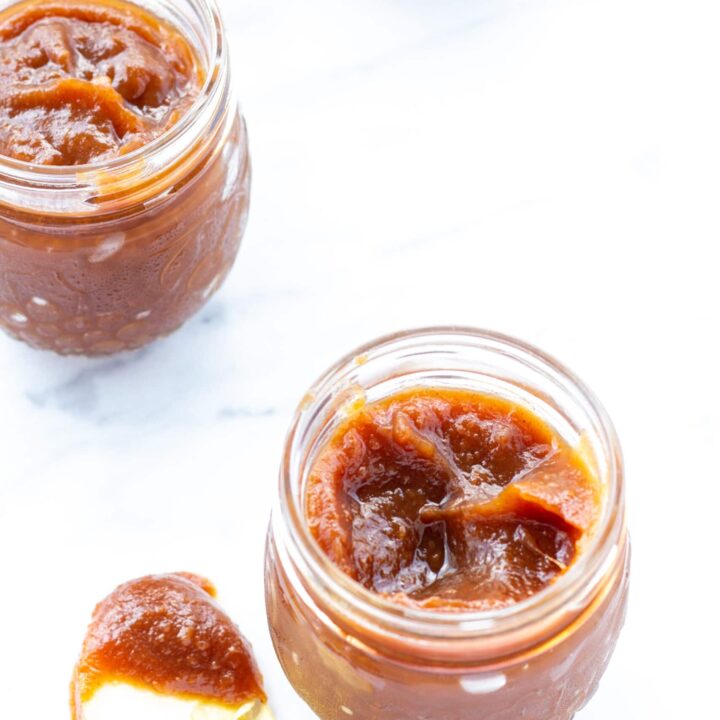 two-jars-of-apple-butter-and-one-apple-slice-dipped-in-apple-butter-on-a-white-counter