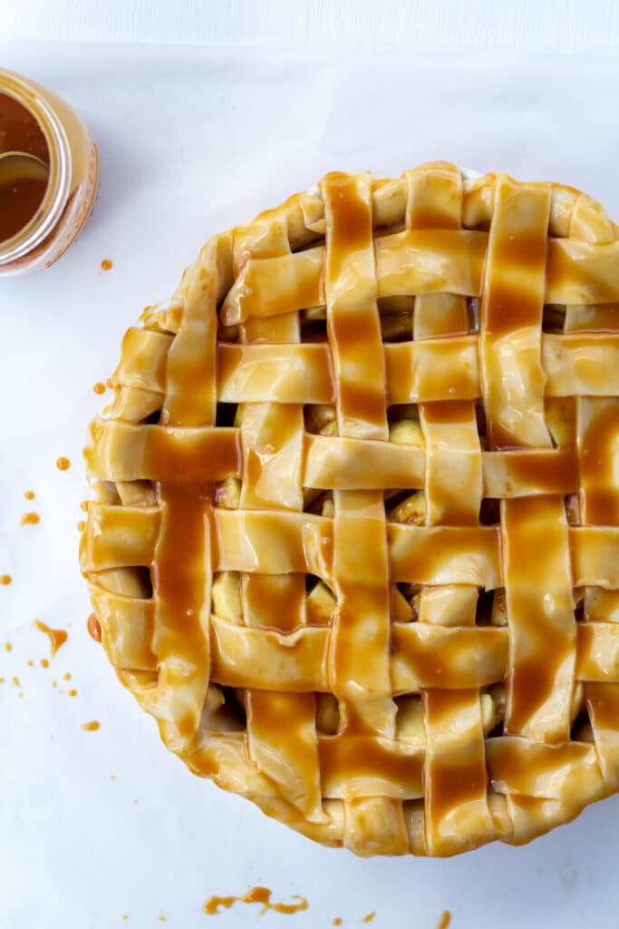 unbaked apple pie brushed with caramel sauce on a white surface